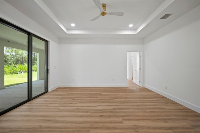 empty room with ceiling fan, a raised ceiling, and light hardwood / wood-style flooring