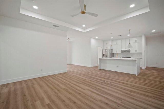 unfurnished living room featuring a tray ceiling, light hardwood / wood-style floors, and ceiling fan