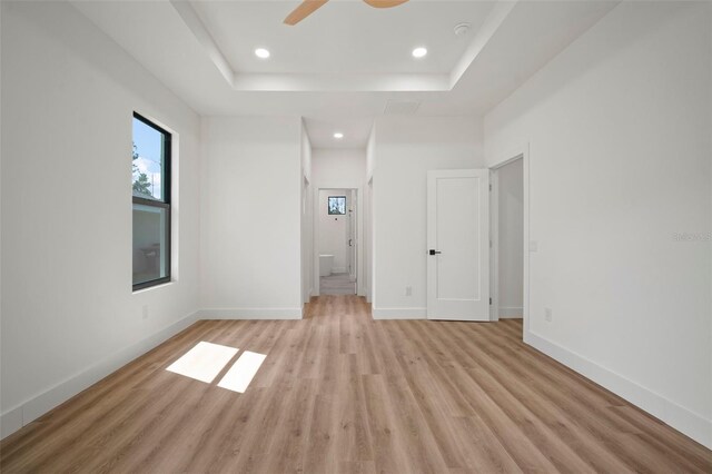 unfurnished bedroom with a tray ceiling, light hardwood / wood-style flooring, ensuite bathroom, and ceiling fan