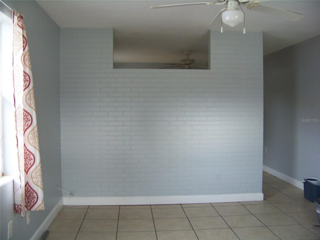 spare room with ceiling fan, brick wall, and tile patterned floors