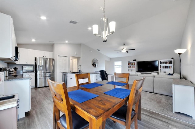 dining room with ceiling fan with notable chandelier, vaulted ceiling, wood-type flooring, and sink