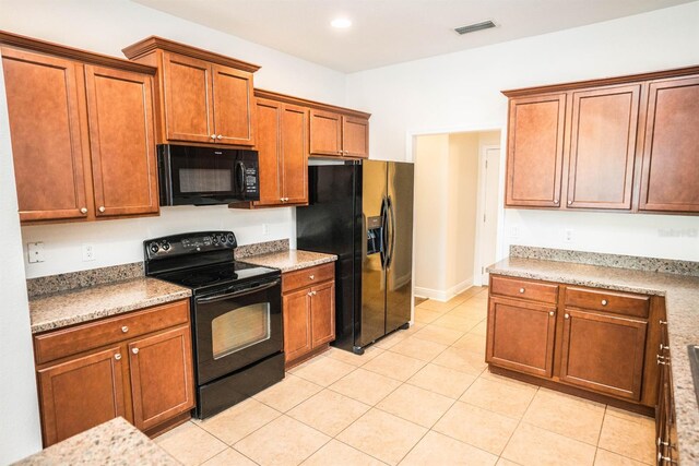 kitchen with black appliances, light stone counters, and light tile patterned floors