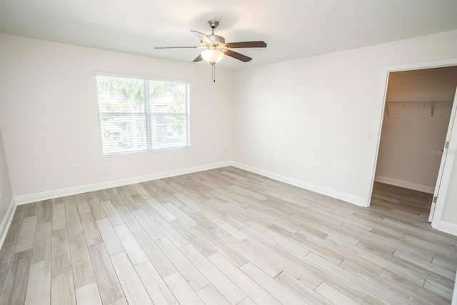 unfurnished bedroom with light wood-type flooring, a closet, ceiling fan, and a spacious closet