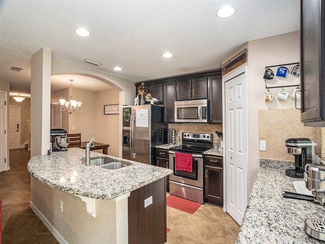 kitchen with appliances with stainless steel finishes, light stone counters, sink, a breakfast bar area, and pendant lighting