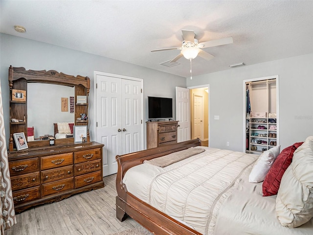 bedroom featuring multiple closets, a textured ceiling, light hardwood / wood-style flooring, and ceiling fan