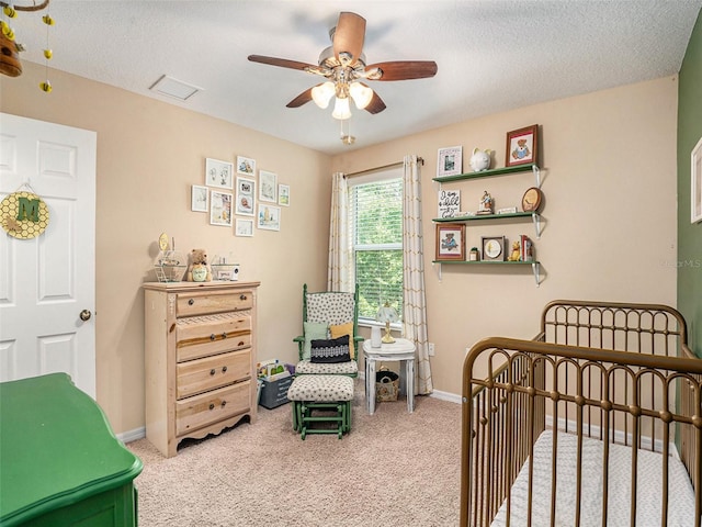 carpeted bedroom featuring a textured ceiling, a nursery area, and ceiling fan