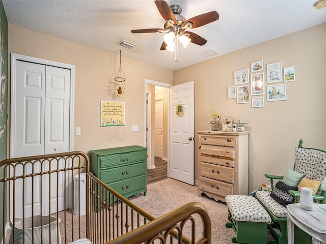 bedroom with a closet, ceiling fan, light colored carpet, and a crib