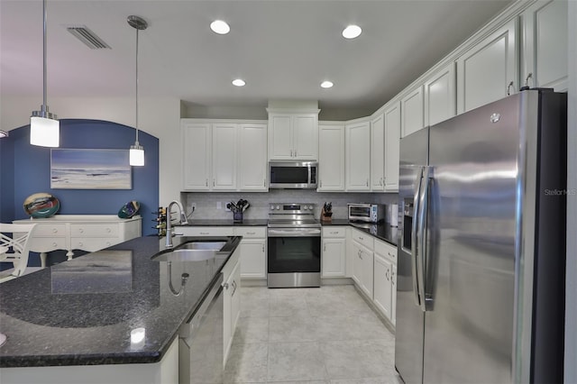 kitchen with white cabinetry, sink, stainless steel appliances, dark stone counters, and pendant lighting