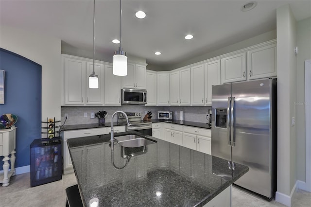 kitchen featuring appliances with stainless steel finishes, decorative light fixtures, white cabinetry, and an island with sink