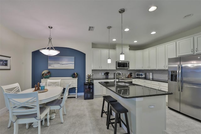 kitchen featuring backsplash, stainless steel appliances, white cabinets, hanging light fixtures, and an island with sink