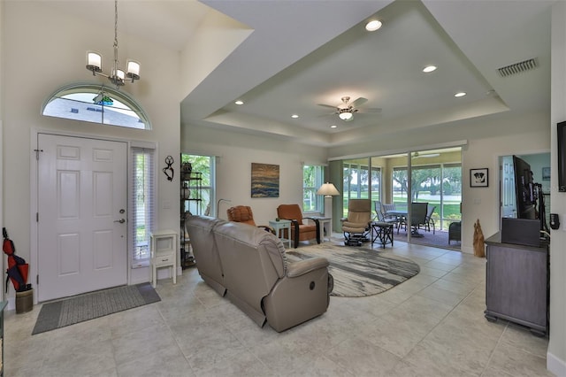 tiled foyer entrance with ceiling fan with notable chandelier, a healthy amount of sunlight, and a raised ceiling