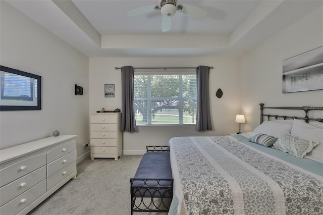 carpeted bedroom with a raised ceiling and ceiling fan