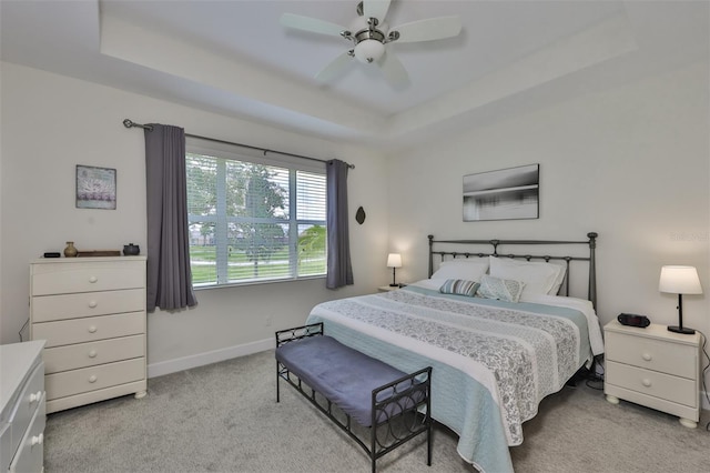 bedroom with light colored carpet, a raised ceiling, and ceiling fan