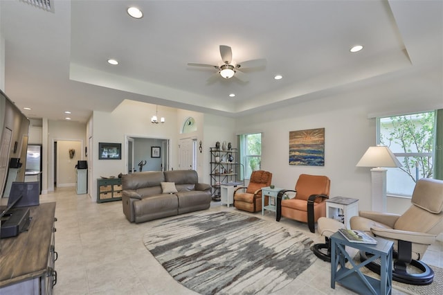 living room with ceiling fan with notable chandelier, a raised ceiling, and light tile patterned floors