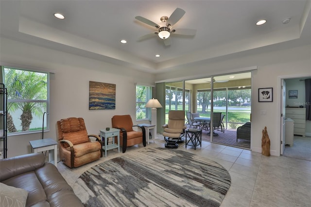 tiled living room with ceiling fan and a raised ceiling