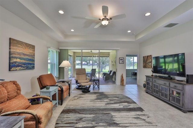 living room with a tray ceiling, ceiling fan, and light tile patterned floors