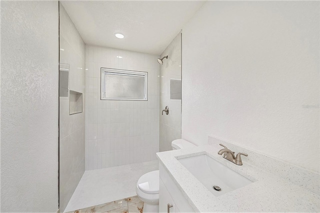 bathroom with toilet, vanity, tile patterned flooring, and tiled shower