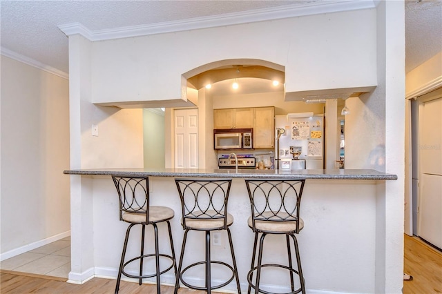 kitchen with a breakfast bar area, crown molding, stainless steel appliances, baseboards, and arched walkways