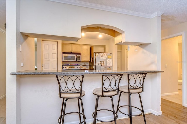 kitchen with a textured ceiling, white appliances, a kitchen breakfast bar, and light hardwood / wood-style floors