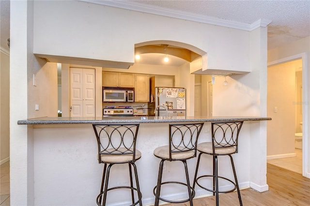 kitchen featuring range, stainless steel microwave, arched walkways, a kitchen breakfast bar, and freestanding refrigerator