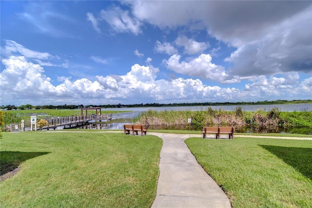 view of property's community featuring a water view, a boat dock, and a lawn