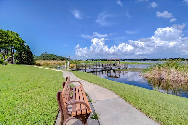 view of property's community featuring a water view, a dock, and a lawn