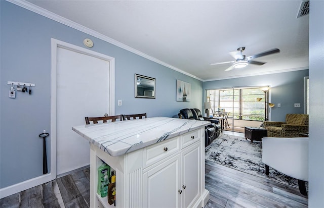 kitchen with ceiling fan, white cabinets, wood-type flooring, a breakfast bar area, and crown molding