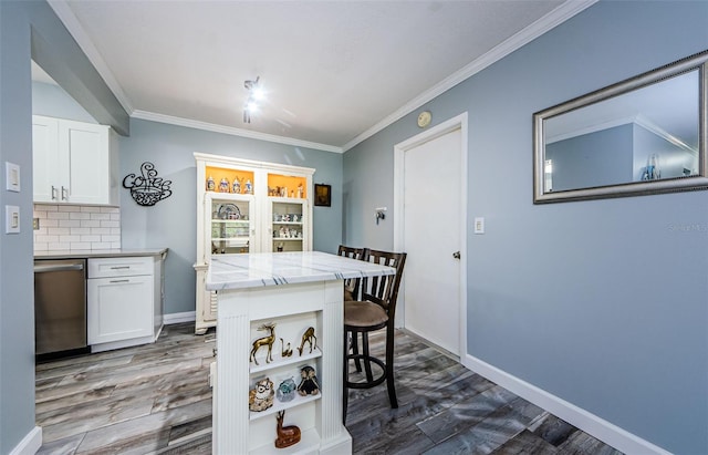 kitchen with white cabinets, a kitchen breakfast bar, decorative backsplash, ornamental molding, and stainless steel dishwasher