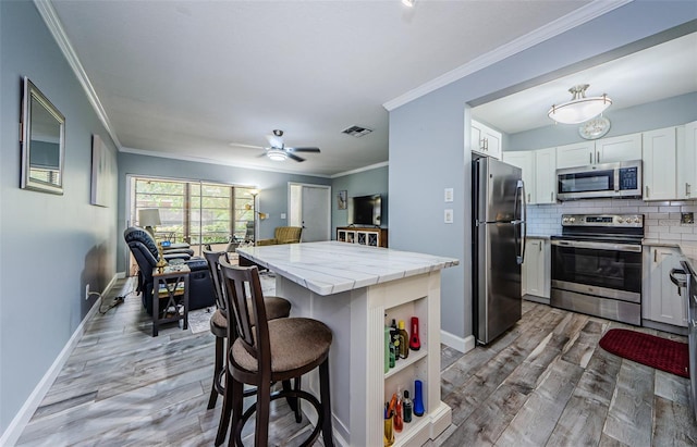 kitchen with white cabinetry, a kitchen island, a breakfast bar area, stainless steel appliances, and hardwood / wood-style floors