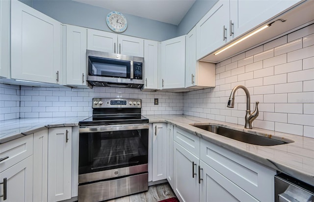 kitchen featuring light hardwood / wood-style floors, sink, white cabinets, decorative backsplash, and appliances with stainless steel finishes