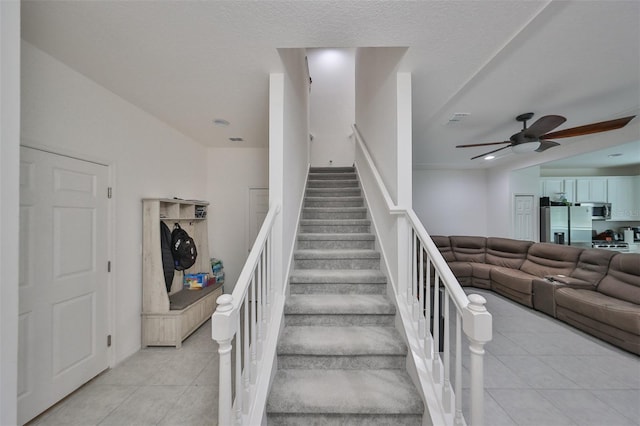 staircase featuring ceiling fan, a textured ceiling, and tile patterned floors