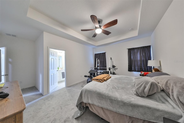 bedroom with a raised ceiling, ensuite bath, carpet floors, and ceiling fan