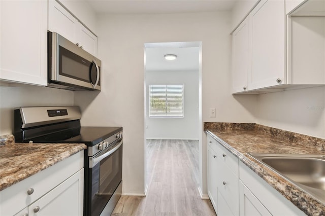 kitchen with appliances with stainless steel finishes, light wood-type flooring, white cabinetry, and sink