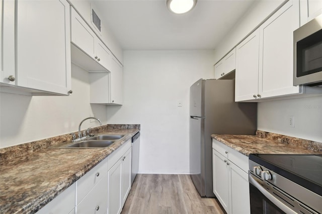 kitchen with sink, light hardwood / wood-style flooring, white cabinetry, stainless steel appliances, and dark stone counters