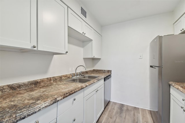 kitchen featuring dark stone counters, sink, white cabinetry, light hardwood / wood-style flooring, and stainless steel appliances