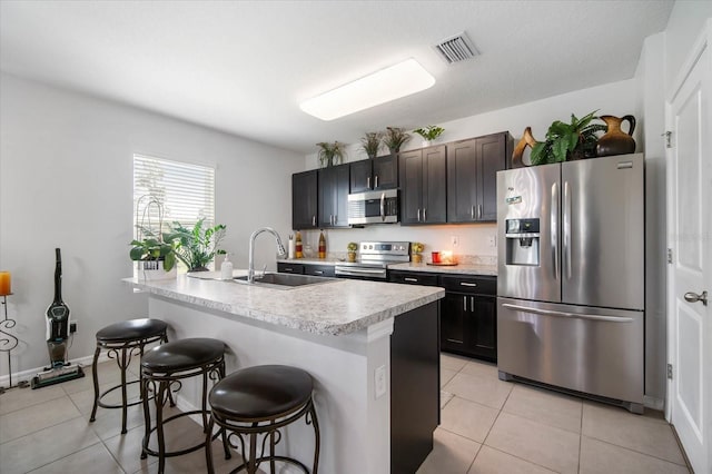 kitchen with a sink, a breakfast bar area, stainless steel appliances, light tile patterned floors, and visible vents