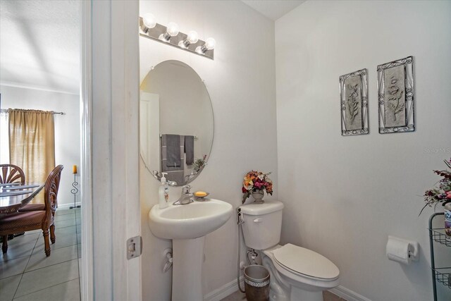 half bath with tile patterned floors, toilet, baseboards, and a sink