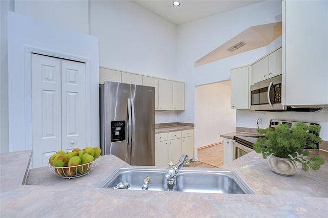 kitchen featuring a towering ceiling, appliances with stainless steel finishes, sink, and white cabinets