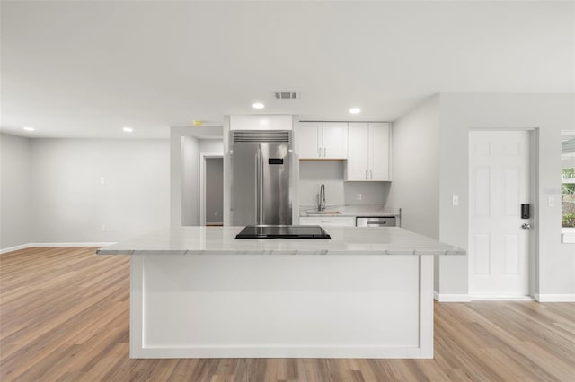 kitchen with light stone counters, light hardwood / wood-style floors, sink, white cabinets, and built in fridge