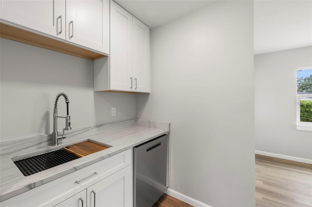 kitchen featuring white cabinets, light stone countertops, light wood-type flooring, stainless steel dishwasher, and sink