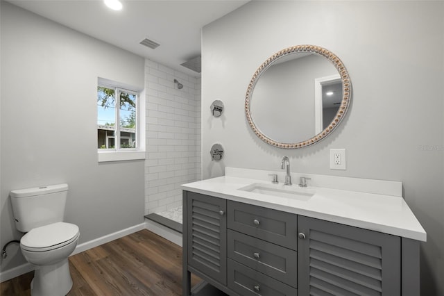 bathroom featuring hardwood / wood-style floors, tiled shower, vanity, and toilet