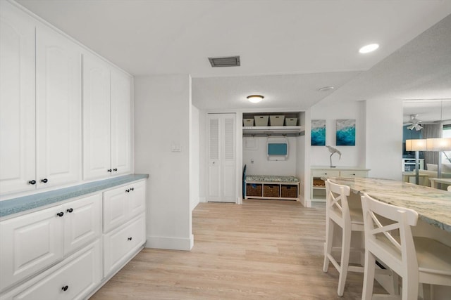 kitchen with white cabinets, ceiling fan, light stone counters, and light wood-type flooring