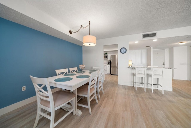 dining area with light wood-type flooring and a textured ceiling