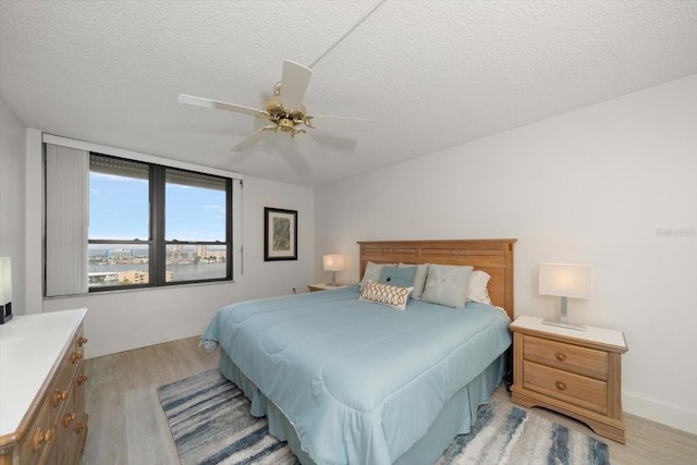 bedroom with ceiling fan, light hardwood / wood-style flooring, and a textured ceiling