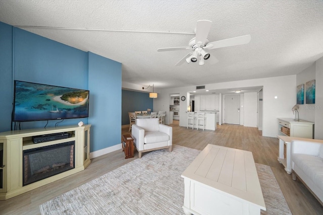 living room featuring ceiling fan, light hardwood / wood-style floors, and a textured ceiling