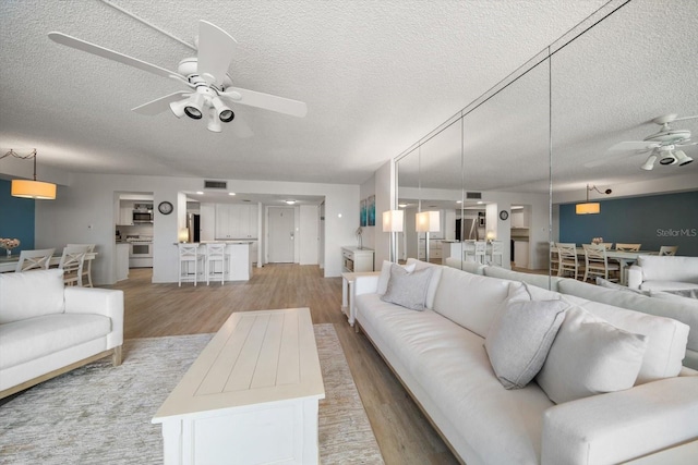 living room with a textured ceiling, light wood-type flooring, and ceiling fan