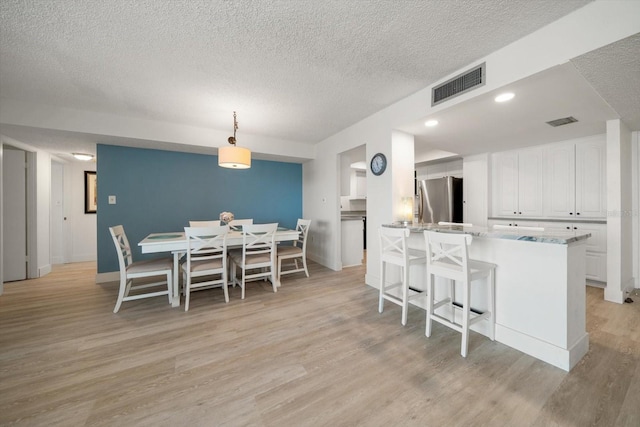 kitchen featuring stainless steel fridge, white cabinetry, light hardwood / wood-style flooring, and pendant lighting