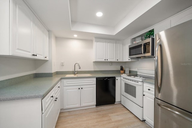 kitchen featuring appliances with stainless steel finishes, a raised ceiling, sink, white cabinets, and light hardwood / wood-style floors