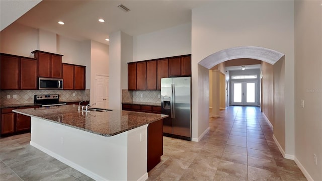 kitchen with french doors, stainless steel appliances, a kitchen island with sink, sink, and tasteful backsplash