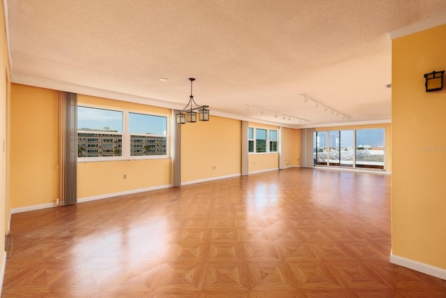 unfurnished living room featuring track lighting, a textured ceiling, plenty of natural light, and a notable chandelier